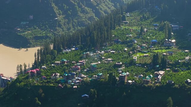 Kasol village with hotels, homes, orchards, dense pine forests, and a reservoir along the Parvati Valley in Himachal Pradesh, India. Aerial orbit drone