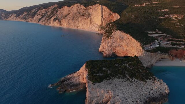 Spectacular drone footage at sunset over Porto Katsiki in Lefkada, Greece. The camera glides above dramatic white limestone cliffs and turquoise waters of the Ionian Sea, revealing one of the Mediterr