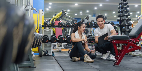 Naklejka premium Asian personal trainer discussing fitness workout plan with woman client in modern gym for healthy lifestyle