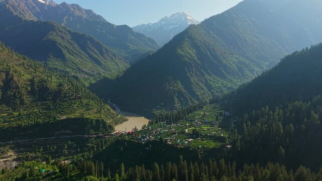 Expansive Parvati Valley with forested mountain slopes, snow capped Himalayan peaks, riverside settlements, and a reservoir near Kasol, Himachal Pradesh, India. Aerial establishing shot