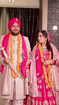 Vertical Shot of Happy Sikh Bride and Groom Wearing Marigold Garlands Walking Together at their Wedding Venue