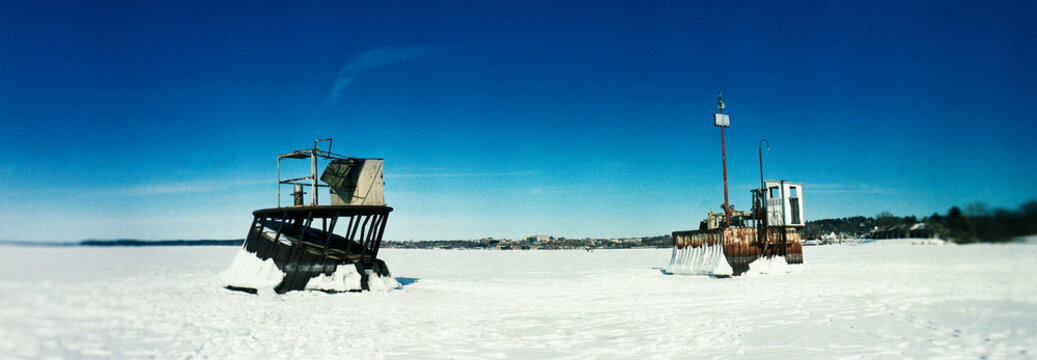 Panoramic view of two industrial water intake structures (often referred to as intake cribs or pump towers) standing out of the completely frozen surface of Lake Champlain, Burlington, Vermont