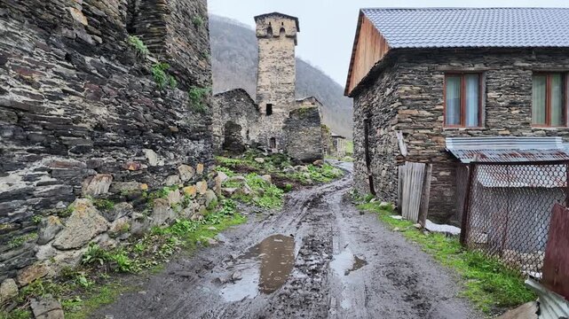 Ancient stone defensive towers in rural mountain village with muddy path, rustic architecture, historical georgian highland heritage, travel destination, Ushguli, Svaneti, Georgia