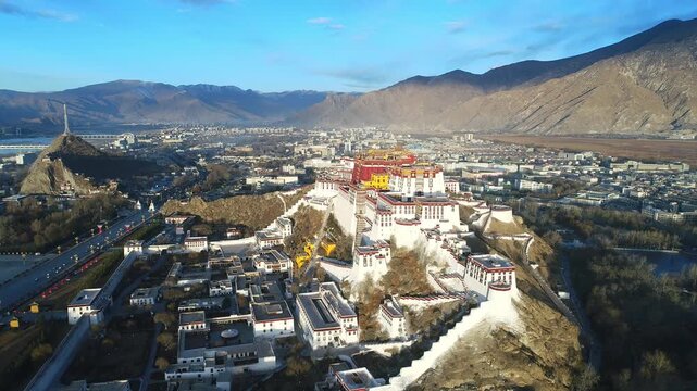 Aerial view of the Potala Palace at sunrise in Lhasa, Tibet, China, with the historic palace on the hill overlooking the city, surrounded by mountains and morning mist under golden light.