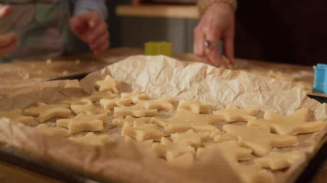 Close up shot of senior grandmother and grandchild placing star-shaped raw cookie dough on baking sheet. Video suitable for family lifestyle campaigns or holiday baking promotions