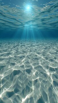 Underwater view of clear ocean water with sun rays penetrating the surface and sandy seabed.