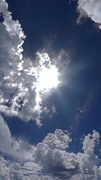 Bright sun shining through scattered clouds in a blue sky.