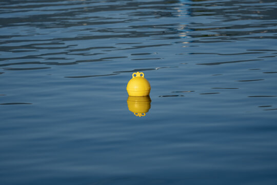 Yellow floating buoy on calm blue sea water with reflection. Minimal marine background, navigation marker and nautical safety concept with ample copy space.