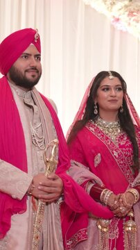 Vertical Shot of Traditional Sikh Bride and Groom Standing on Reception Stage with Floral Background