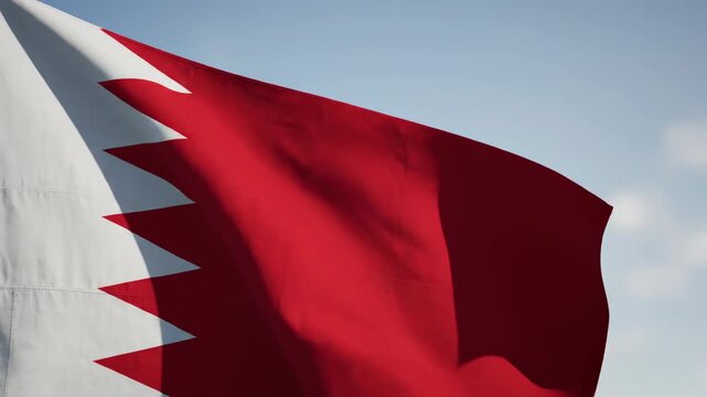 Bahrain flag closeup crane shot, red white serrated zigzag triangles fabric rippling gently waving descending pan blue sunny sky white clouds background footage. National pride patriotic theme