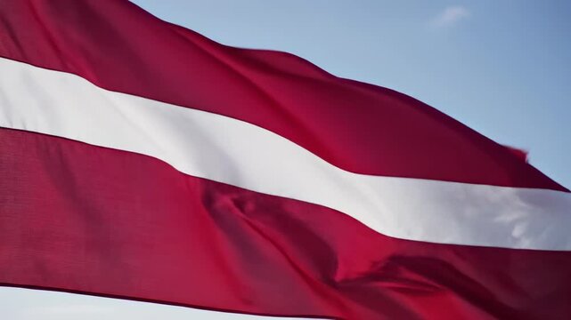 Latvia national flag waving in slow tracking medium close-up, pale blue sky, distinctive deep carmine red field, narrow white horizontal stripe through center, textured silky fabric, fluid motion