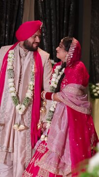 Vertical Shot of Romantic Punjabi Newlyweds Holding Hands After Varmala Ceremony In Elegant Hallway