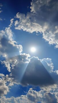 Bright sun shining through fluffy white clouds in a blue sky.