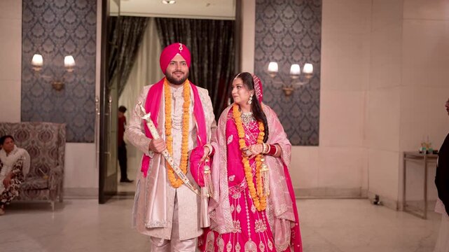 Happy Sikh Bride and Groom Wearing Marigold Garlands Walking Together at their Wedding Venue