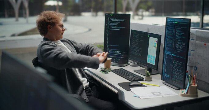App Engineer Alternates Between Coding and Quick Wrist Stretches at a Multi-screen Desk, Debugging Mobile Ui Screens, Source Code, Notes, Analytics in  Office for Product.  Working Using Computer