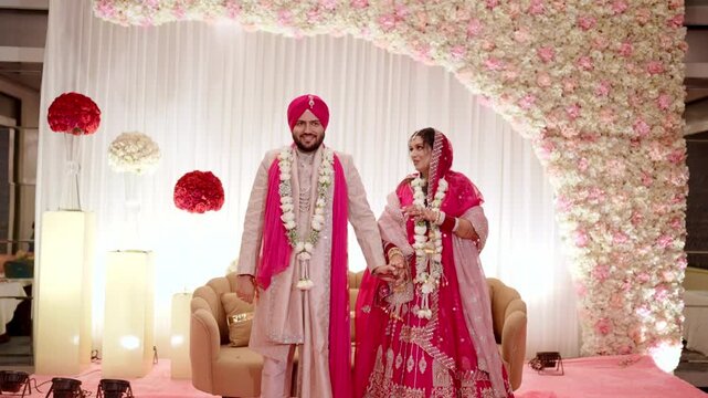 Sikh Bride and Groom Holding Hands Up After Varmala Ceremony with Elegant Stage Decor