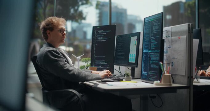 Focused App Developer Settles Into Work, Typing and Scanning Source Code on Stacked Monitors While Comparing a Mobile Ui Task Notes and Data Dashboards in  Tech Office.  Working Using Computer