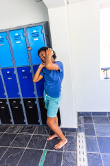 Naklejka premium African American teen leaning in locker room adjusting hair barefoot in blue tee near padlock