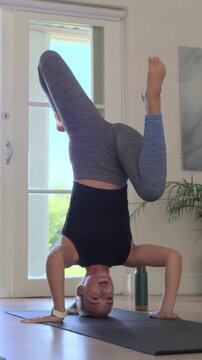 Vertical video: Doing headstand woman in black tank on mat at home cycling rolling kneeling smiling