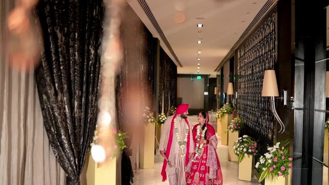 Happy Sikh Bride and Groom Walking through an Elegantly Decorated Hallway After their Wedding Ceremony
