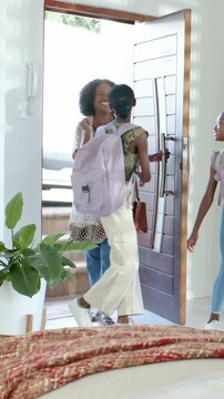 Vertical video: Opening door mom coming with mesh bag hugging girls with packs closing door at home