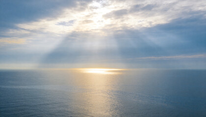 Obraz premium Showing sunlit ocean patch creating reflection over horizon at sea, with clouds and sunbeams
