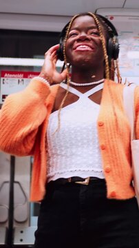Black female technology user in great mood enjoying music in headphones while standing in metro car, using public transport. Carefree happy young woman with vitiligo feeling rhythm oof song in earbuds