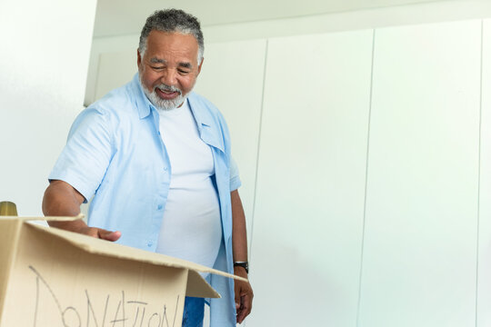 Senior African American man in blue shirt watch smiling, sorting donation box by closet, copy space