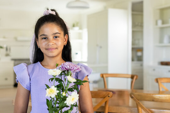 African American teen girl standing in kitchen wearing lilac dress with scrunchie, holding flowers