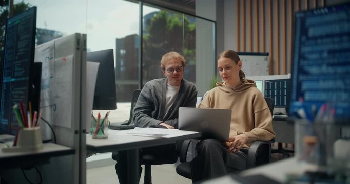 Young Female Engineer Consults Male UI Designer at a Laptop, Mobile Ecommerce Work, AI Personalization, API cybersecurity Checks and Interface Fixes as Code Monitors Glow in a Modern App Office.