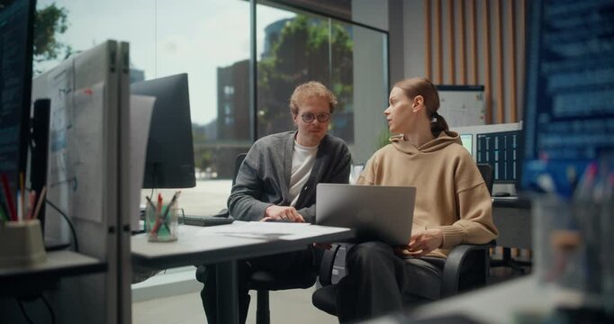 Female Developer and Male Designer Discuss  Mobile Ecommerce App, Using Laptop, AI Drive, Data and Security Fixes as Code Dashboards Span a Busy Modern App Office. Handheld Shot