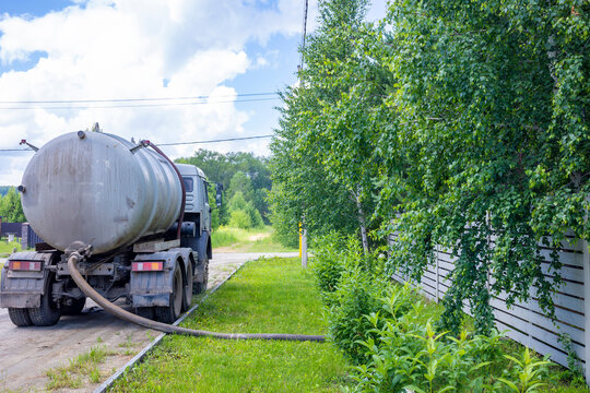 Vacuum truck pumping septic tank with long suction hose near wooden fence. Concept: septic service 