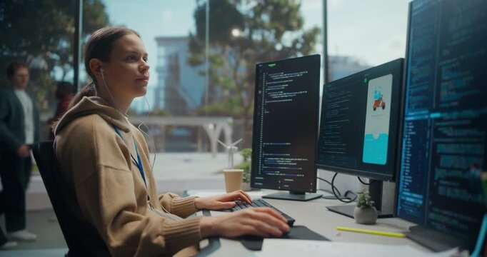 White Female Programmer Wearing Earphones Typing Code on Multiple Computer Screens by Window in Sunny Modern Office, Building Delivery App Interface and Engineering Backend Software Solution