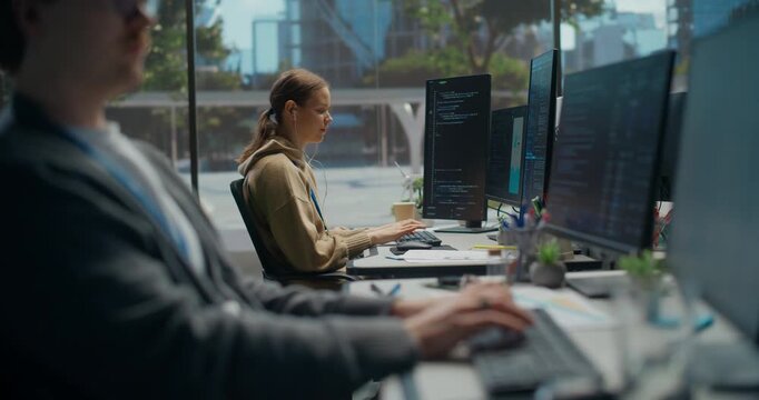 White Male Developer Types Backend Code on Screens in Office, While a Female Engineer Builds an Ai Cybersecurity App Nearby, Highlighting Startup Collaboration and Digital Innovation.