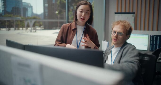 Handheld View: Asian Woman Developer Gestures While Explaining Api Structure and Encryption Updates to a Redhead Male Engineer, Brainstorming App Optimization in a Software Video Game Dev Office.