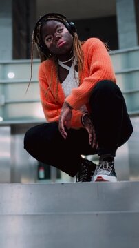 Thoughtful female in casual wear listen to music in headphones while sitting in subway station indoors. Stylish and fashionable young woman with vitiligo skin in wireless earphones. Slow motion
