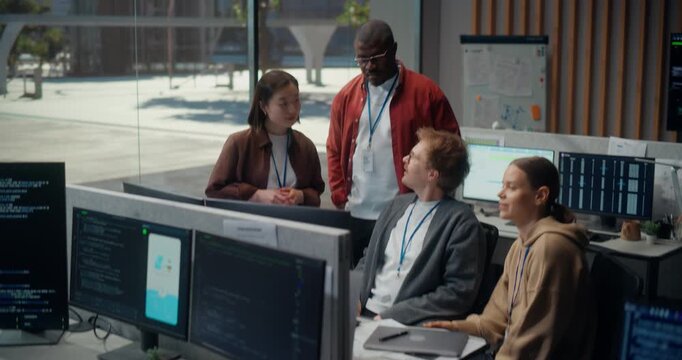 Diverse Developer Crew Meeting, Talk about App Code on Screen in Office: Seated White Man Points While a Woman Colleague Responds, Teammates Discuss AI, UX and Cybersecurity Strategy.