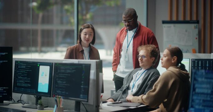 Diverse Team of Young Software Developers Gathers Around Screens in a Modern Office, Discussing Mobile App Code, Ui Design and Cybersecurity Strategy During a Collaborative Startup Project Meeting.