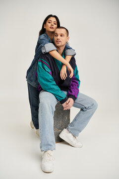 A beautiful young couple poses in fashionable outfits, radiating love and connection in a studio.