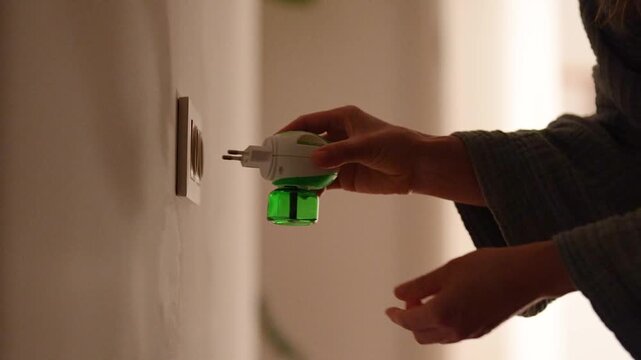 Close up hands installing refill liquid into electric mosquito repellent device and plugging into wall socket. Household fumigator setup for indoor mosquito protection for comfortable night sleep.