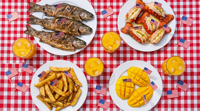 Above View 4th of July Food Spread with Grilled Fish, Lobster Rolls, Potato Wedges, Mango Halves and Refreshing Drinks on Checkered Tablecloth with Patriotic American Flags