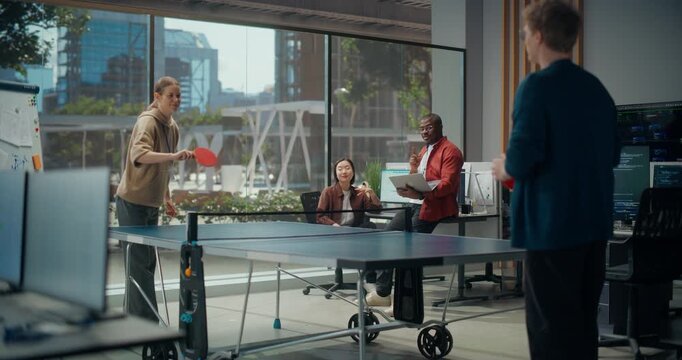 Female Programmer Wins Table Tennis Game Against Male Coworker in Vibrant Tech Office as Black Developer Holding Laptop and Asian Colleague Applaud, Chatting About App Coding, Cybersecurity Design.