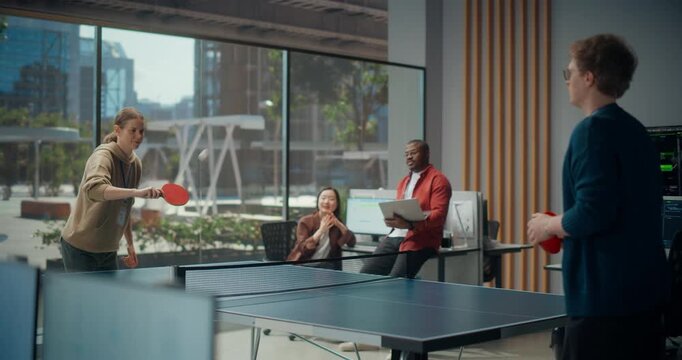 Female and Male Coders Play a Friendly Table Tennis Match in a Modern Office While a Black Male Engineer and Asian Female Developer Discuss App Coding, Cybersecurity, Ux and Software Optimization.