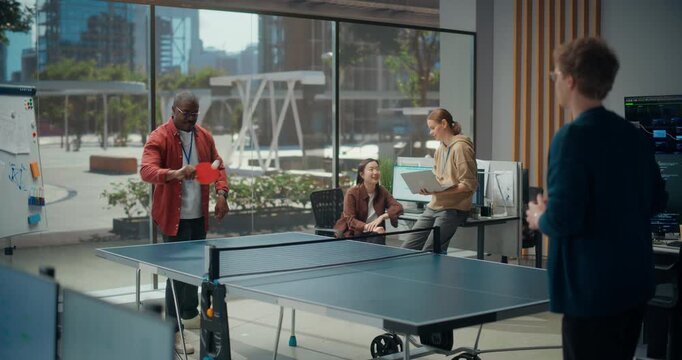Two Male Engineers Rally a Ping Pong Match During a Break While a Black Female and White Female Software Developer discuss App Coding, Cybersecurity, Typing Workflow and Ux Sprint in a Modern Office.