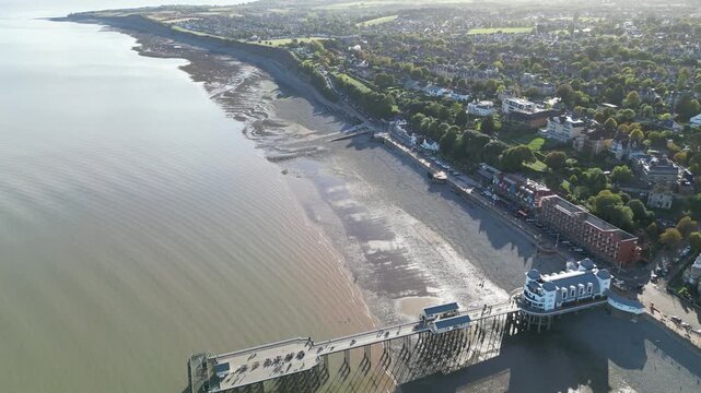 4K Aerial Drone Panning Shot of Penarth Pier Extending Over Calm Sea with Sandy Beach, Waterfront Buildings, and Coastal Town Under Clear Sky, Penarth, Cardiff, Wales, United Kingdom