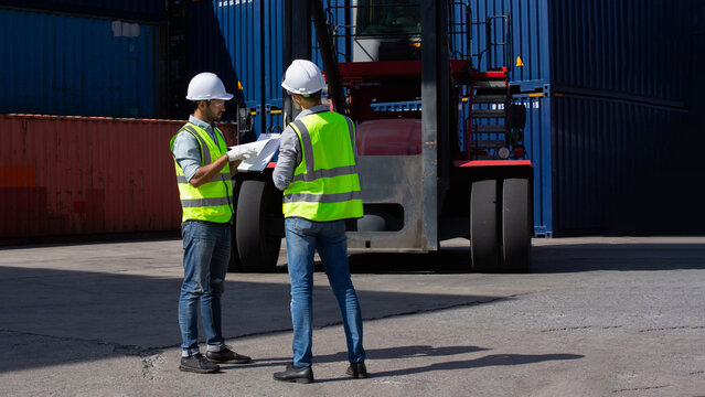 Serious business unfolds beside powerful forklift within vast outdoor shipping container yard as two professionals examine logistics paperwork during critical inspection assessment.
