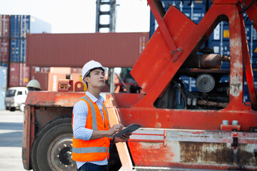 Serious technician meticulously examines Kalmar forklift within busy container yard during equipment inspection and logistics operations assessment – focused maintenance work. © AU USAnakul