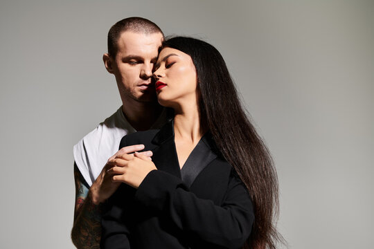 A beautiful couple dressed in fashionable clothes shares an intimate moment in the studio.