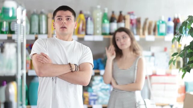 Spouses yell at each other in sales area of household store. Angry and stubborn guy and girl are indignant and swear, family conflict. Couple is arguing and yell at each other