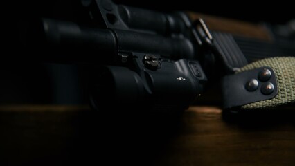 Obraz premium This close up captures the tactical flashlight secured to the barrel assembly of a firearm resting on a wooden surface emphasizing the matte finish and integrated design of the accessory